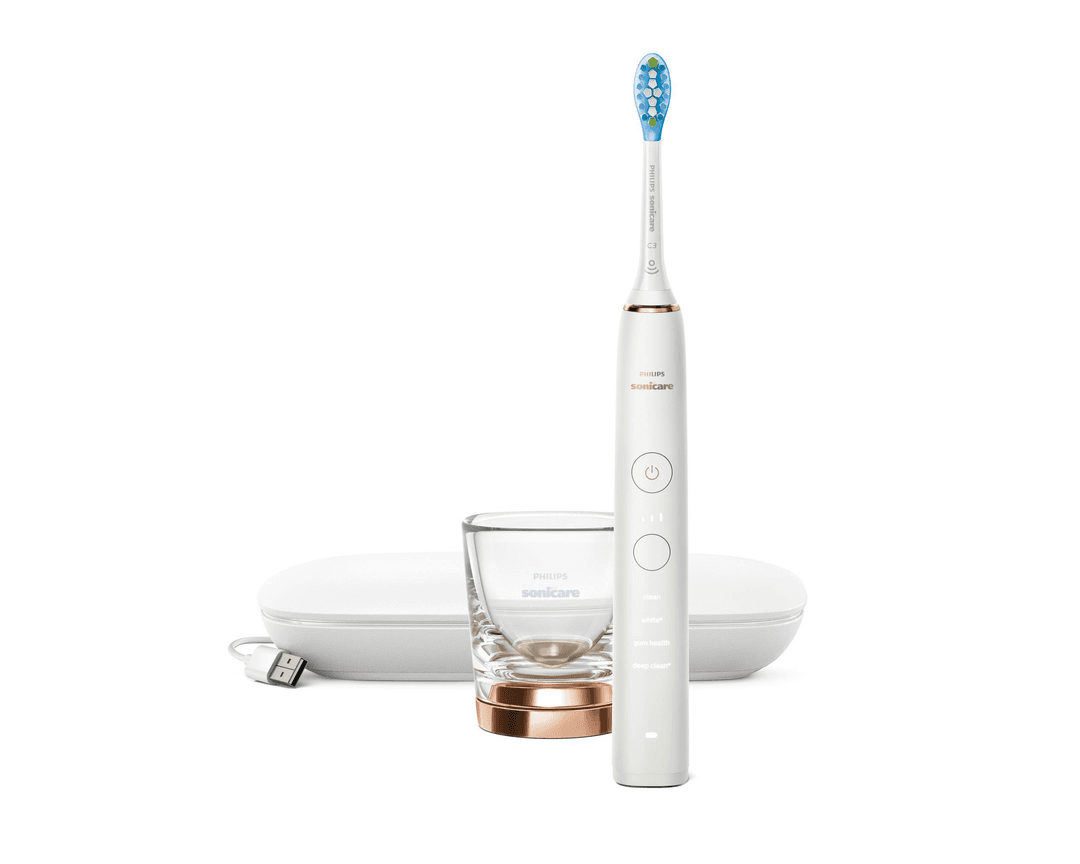 Eine weiße elektrische Zahnbürste von Philips Sonicare, Ladestation, Glas und Ladekabel auf weißer Oberfläche.